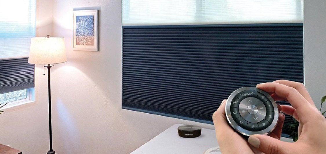Hand holding a camera lens in a bright room with a floor lamp and window blinds