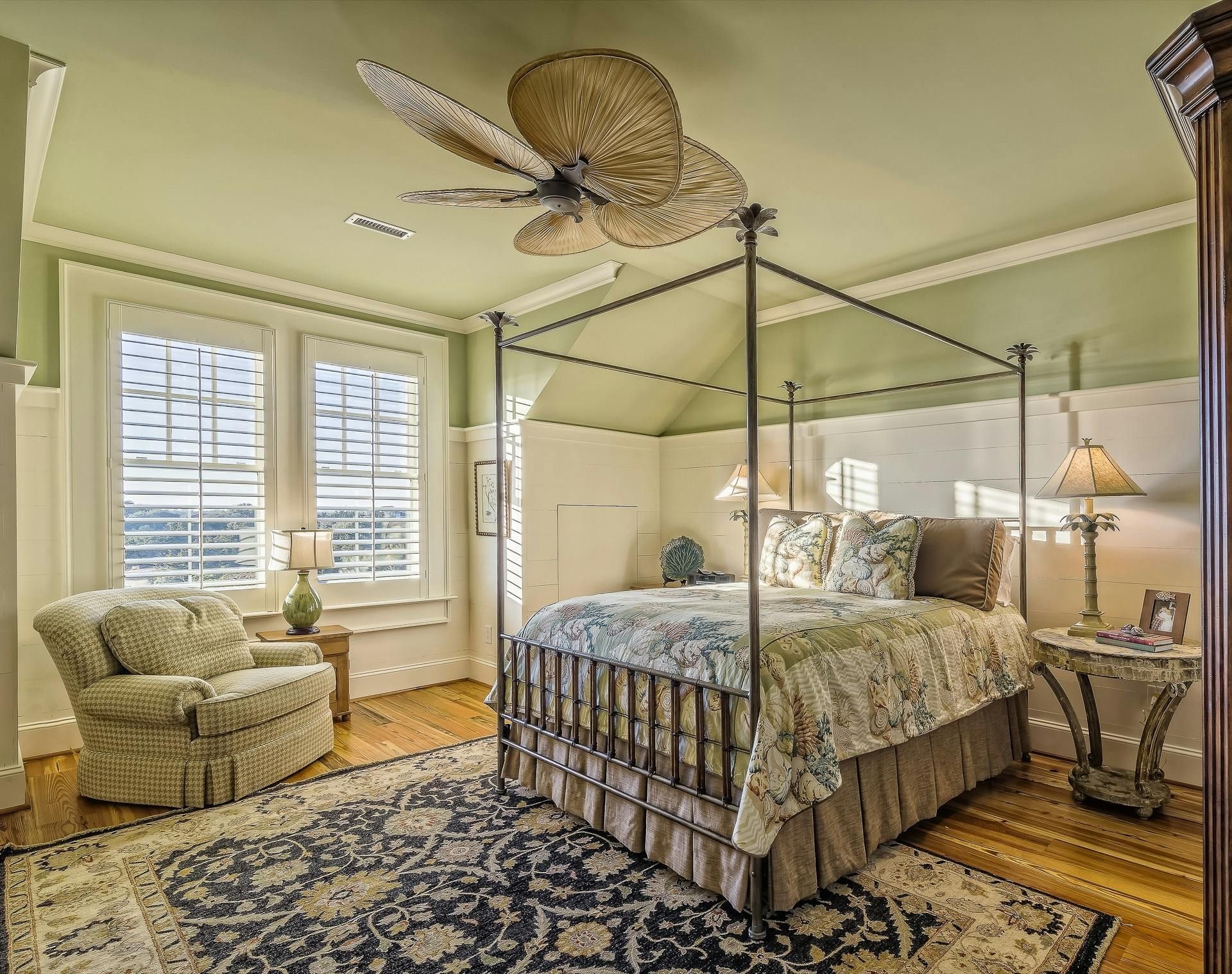 Elegant bedroom with four-poster bed, patterned rug, armchair, and ceiling fan under a bird-shaped light fixture