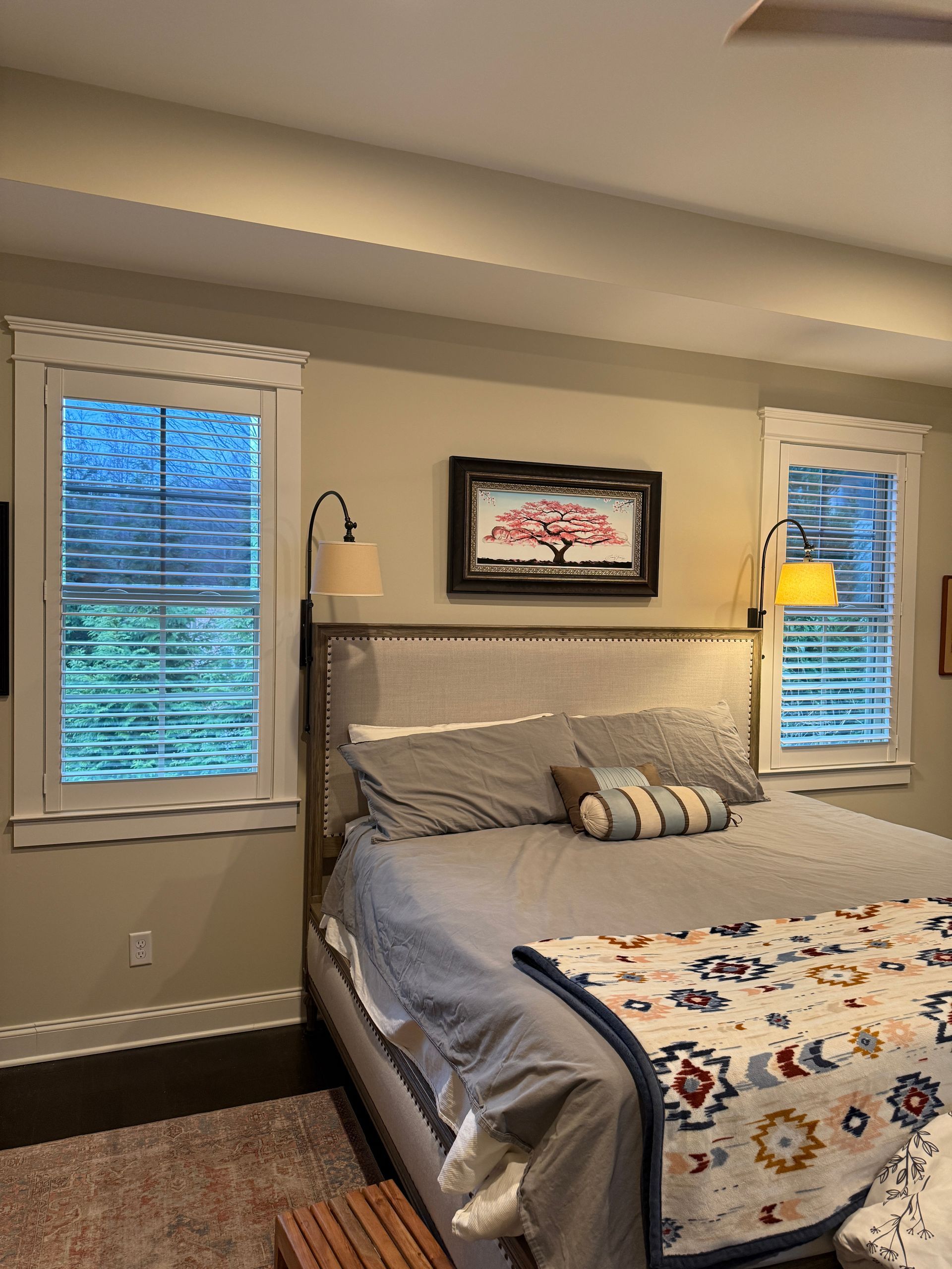 Cozy bedroom with a bed, floral quilt, striped pillows, two windows, and framed wall art.