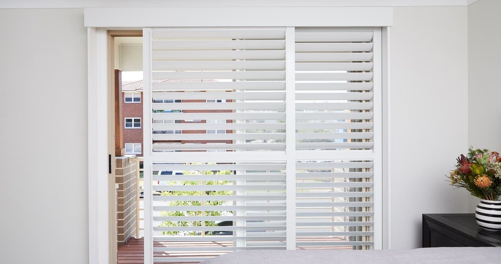 White plantation shutters over sliding glass doors in a bright room with a plant on a dark side table.