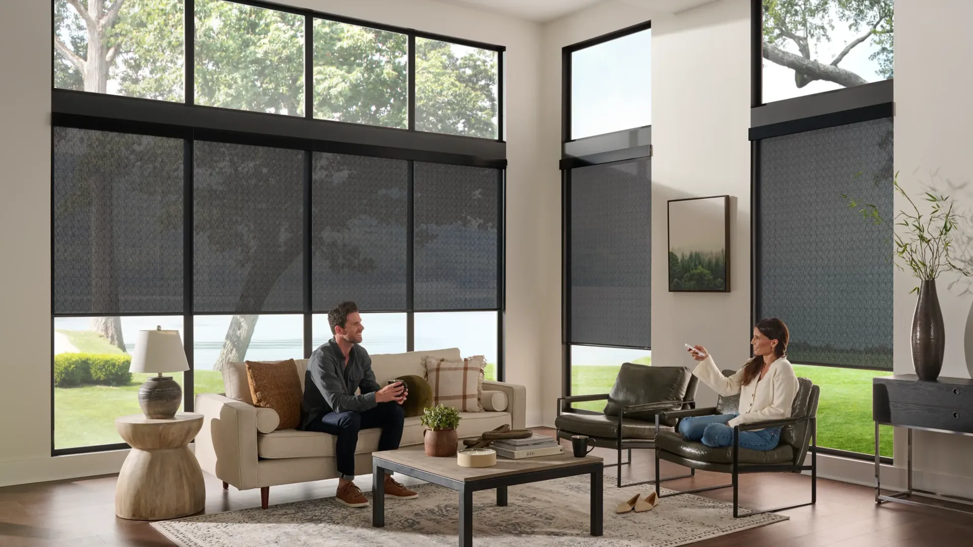 Two people relaxing in a bright modern living room with large windows and blinds