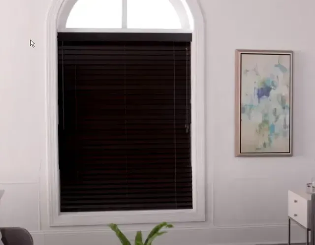White room with arched window, dark blinds, framed floral art, and a small plant in the foreground