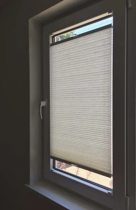 Closed window blind in a dim room, with a white window frame and pull handle.