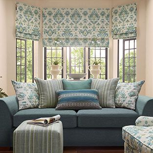 Blue sofa in a bright bay window room with patterned floral blinds and teal patterned pillows