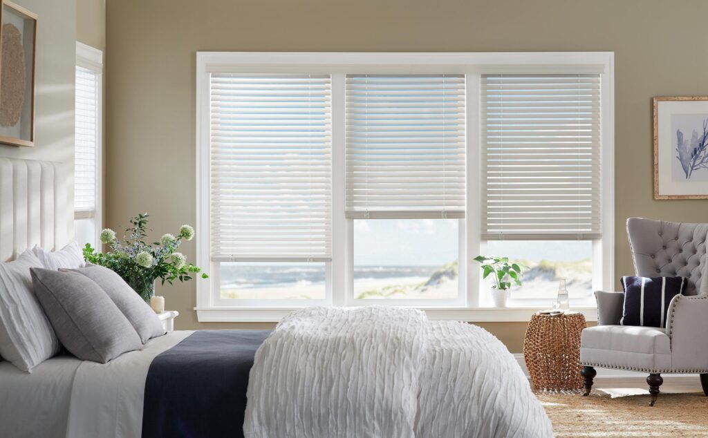 Bright bedroom with bed, large window blinds, and a gray armchair by the wall