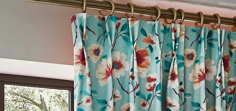 Floral turquoise curtains on a window beside a white wall