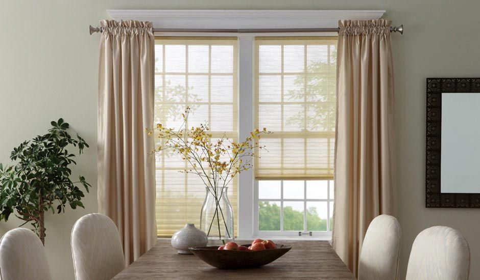 Dining room with beige curtains, a wooden table, white chairs, and a vase of yellow flowers by a bright window