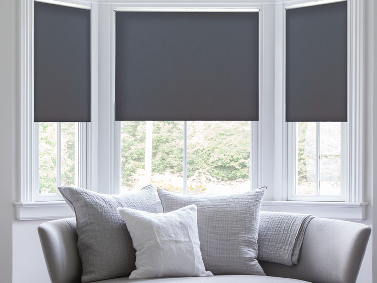 Gray window shades above a light gray sofa with white pillows in a bright bay window nook