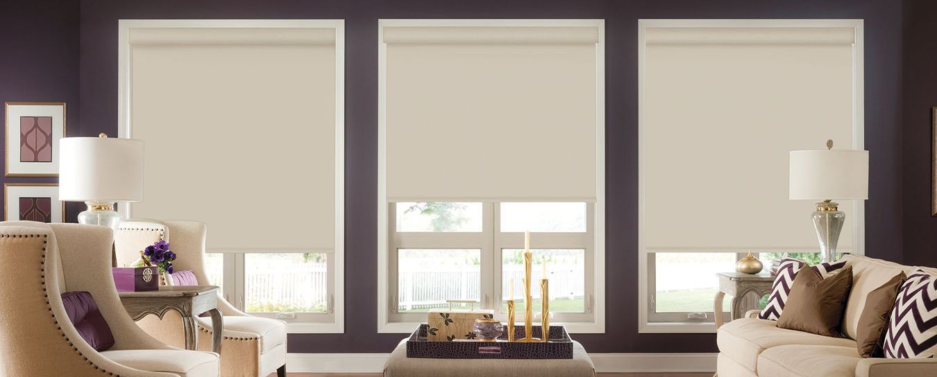 Modern living room with three windows, beige shades, and matching armchairs by a coffee table