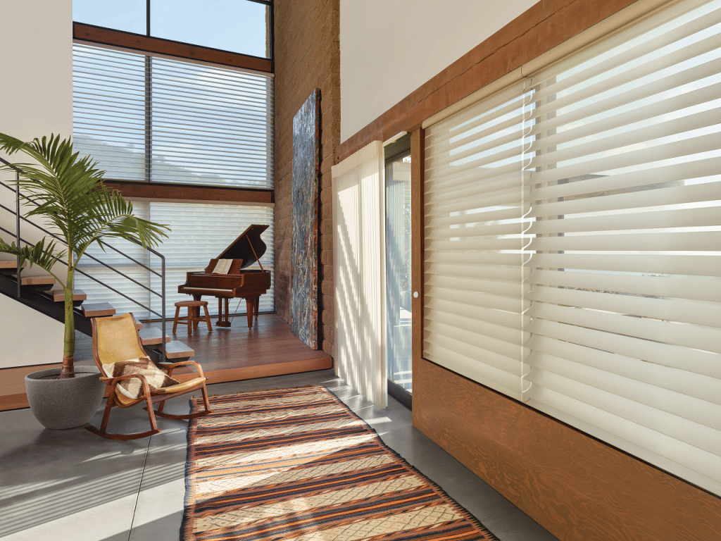 Modern living room with a grand piano, wooden accents, large windows, and striped sunlight on the floor