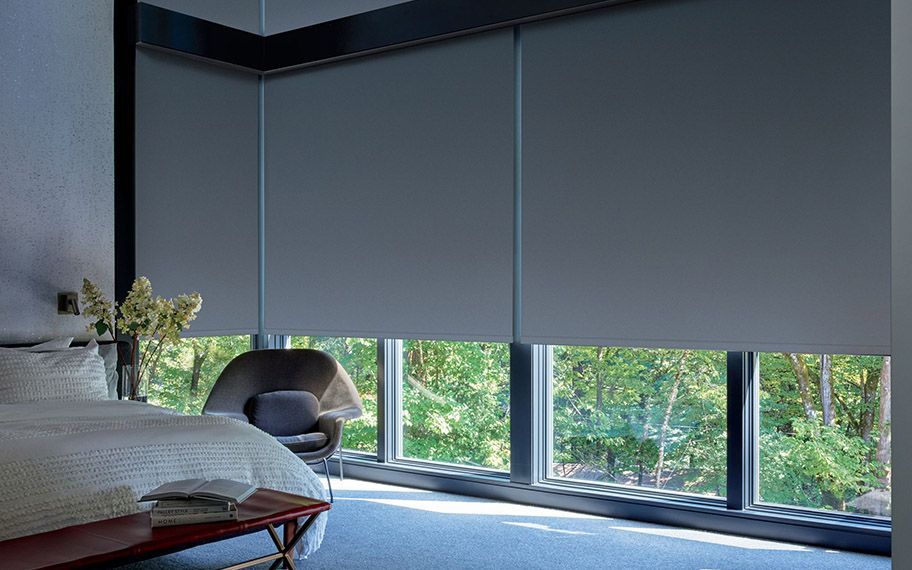 Bedroom with gray roller blinds, a bed, chair, and window view of greenery