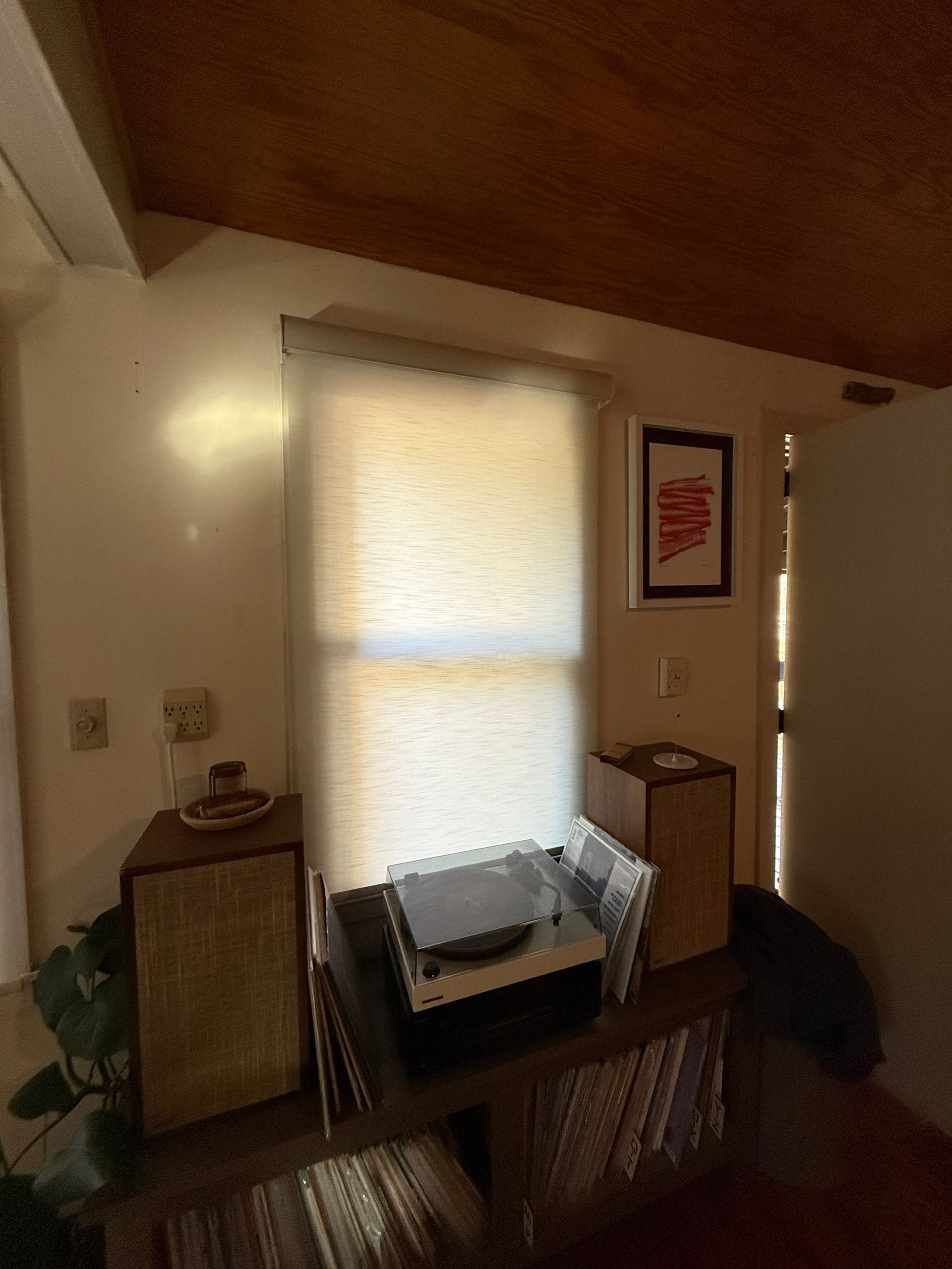 Cozy room with a window, wooden ceiling, small table, cabinet, and framed wall art.