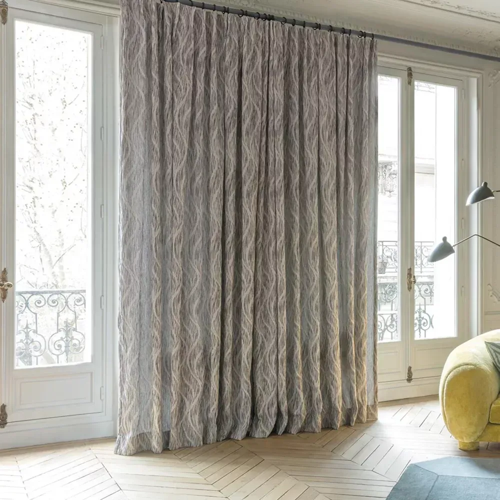 Gray patterned curtains covering tall windows in a bright living room with a yellow chair and floor lamp