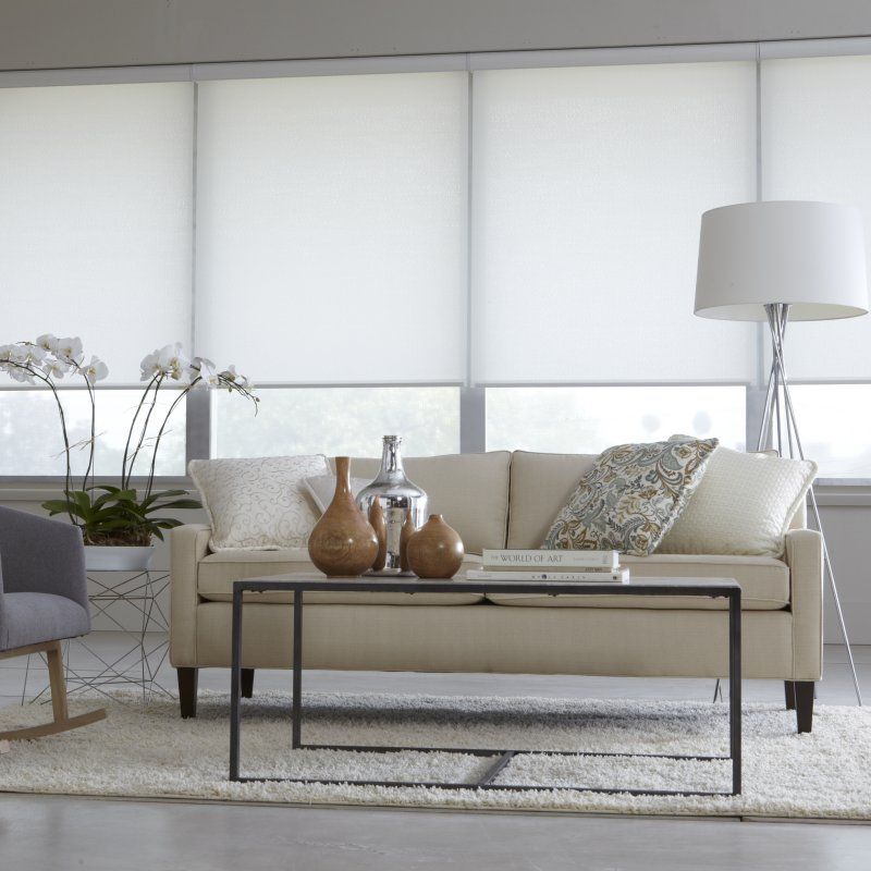 Modern living room with beige sofa, black coffee table, white blinds, floor lamp, and decorative vases