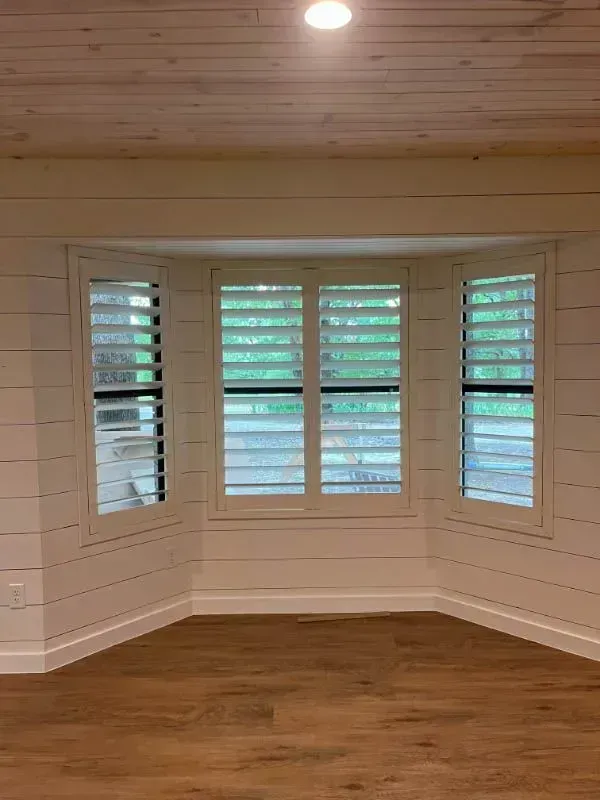 Empty white bay window room with wood floor and plantation shutters