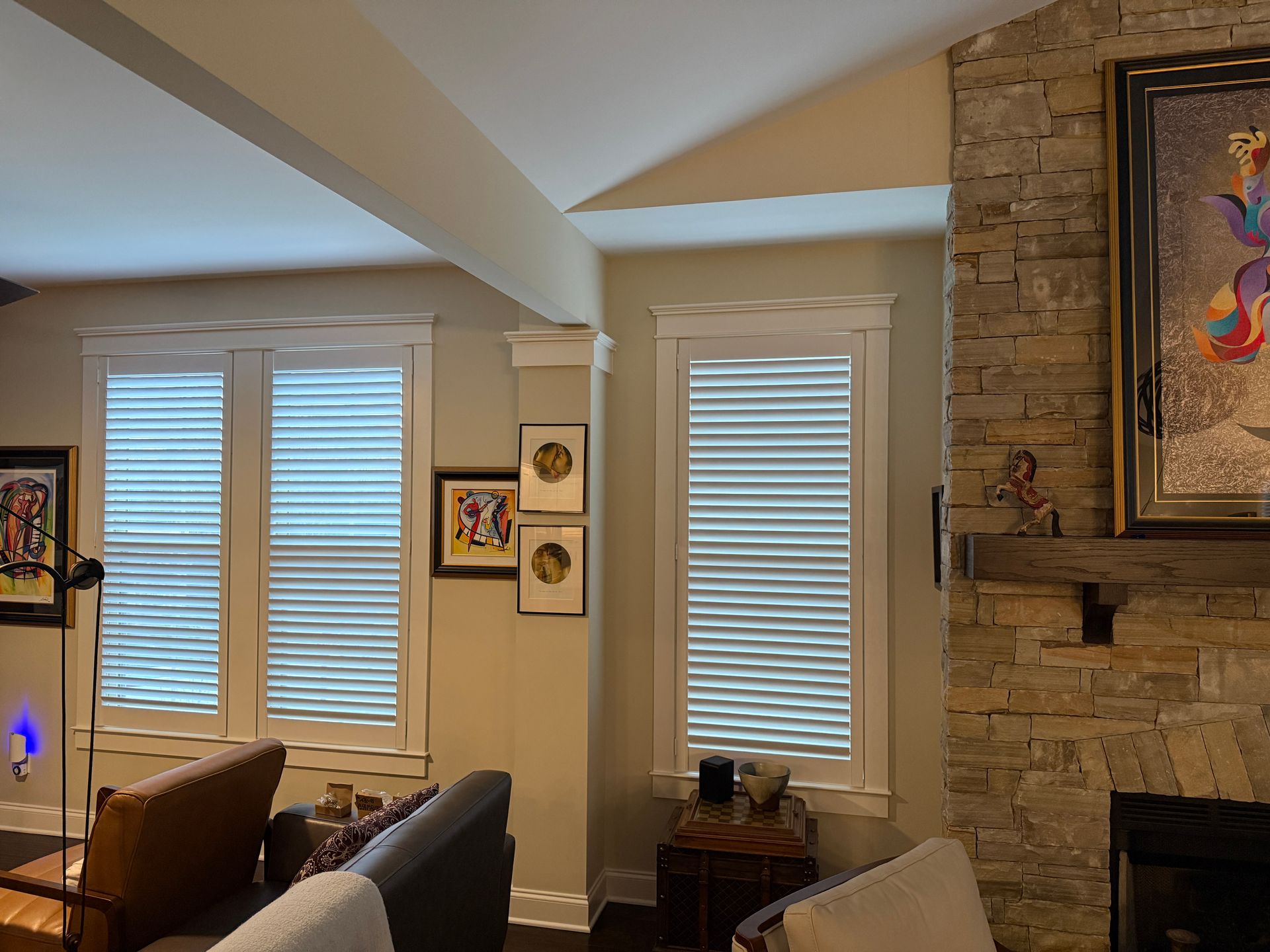 Living room with tall windows, stone fireplace, and framed artwork on beige walls