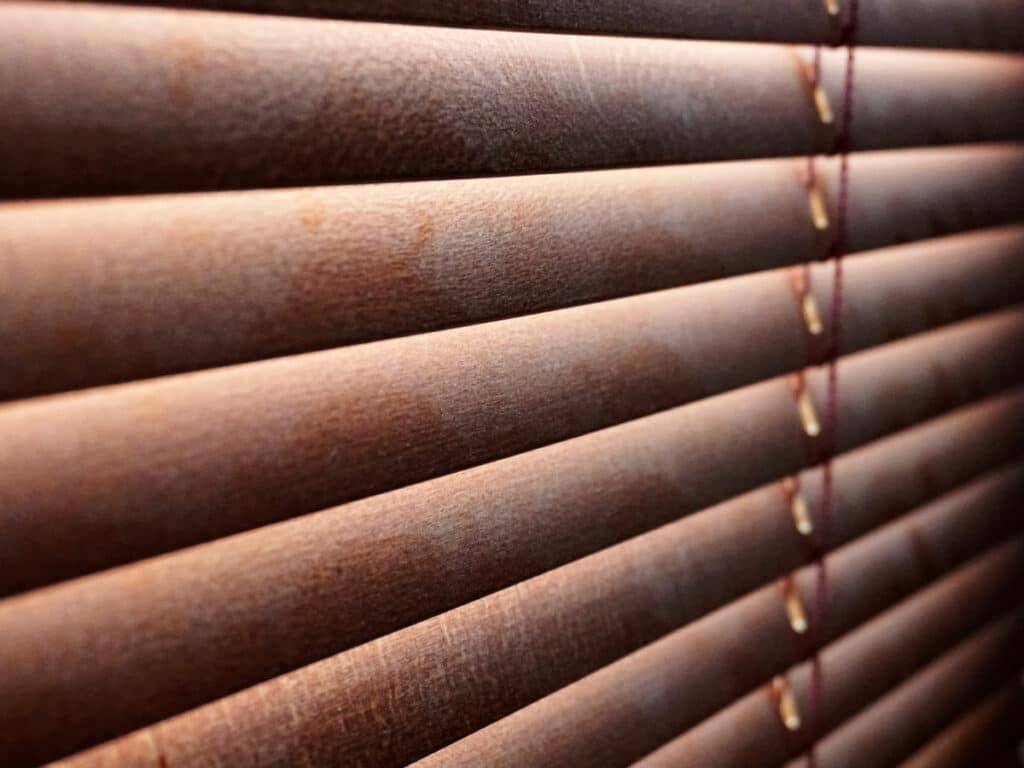 Close-up of brown window blinds with slats angled downward and light filtering through