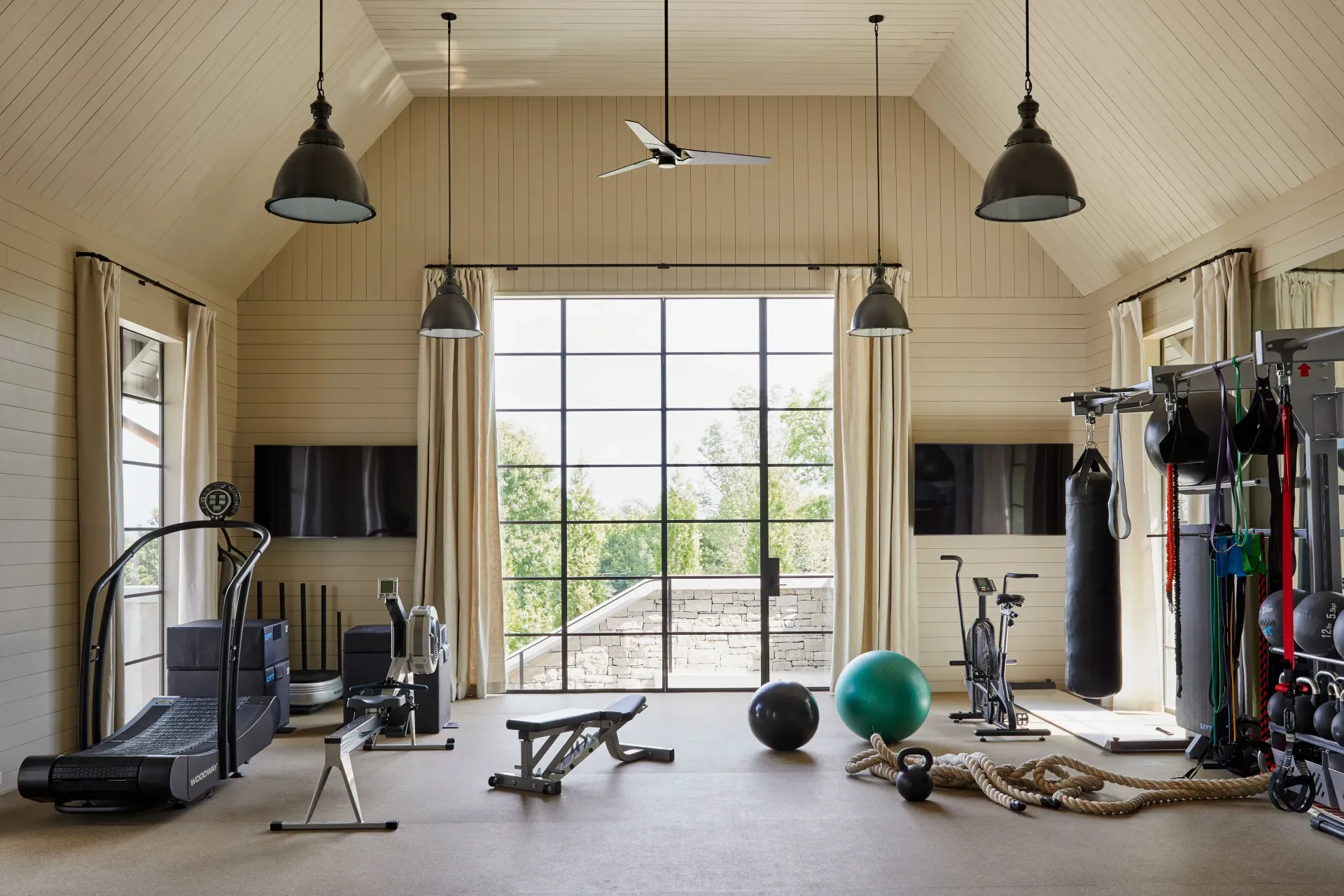 Bright home gym with treadmill, weights, exercise ball, and large glass doors opening to greenery