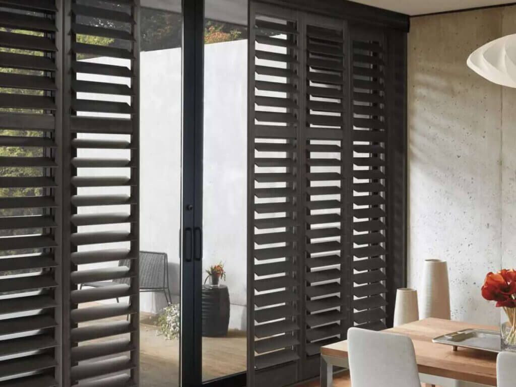 Modern dining room with dark louvered sliding doors opening to a balcony and a table with flowers and candles.