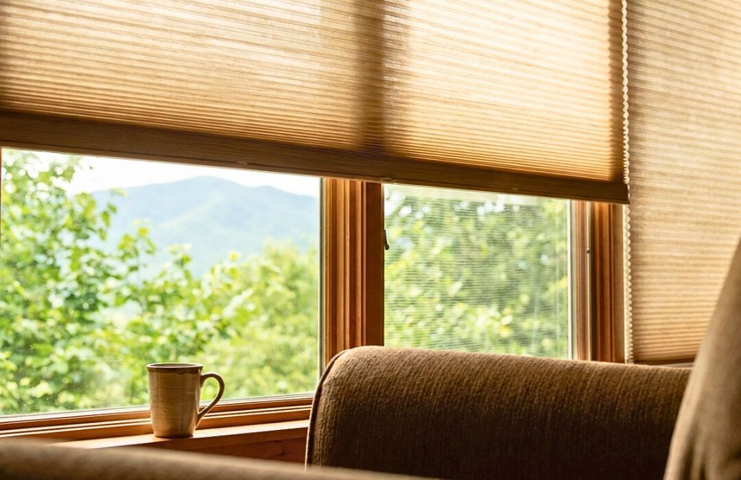 Cozy window seat with a mug on the sill, bamboo blinds, and a green mountain view outside.