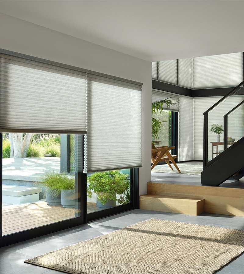 Bright modern living room with sliding doors, woven blinds, staircase, and patio view.