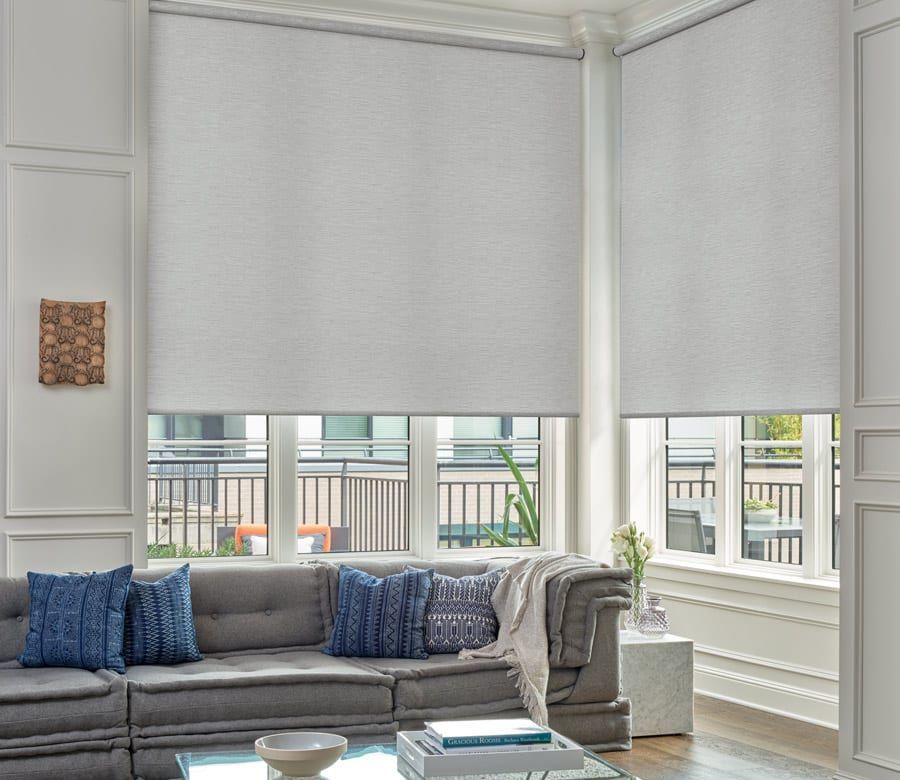 Bright living room with gray sofa, blue pillows, coffee table, and large windows with blinds