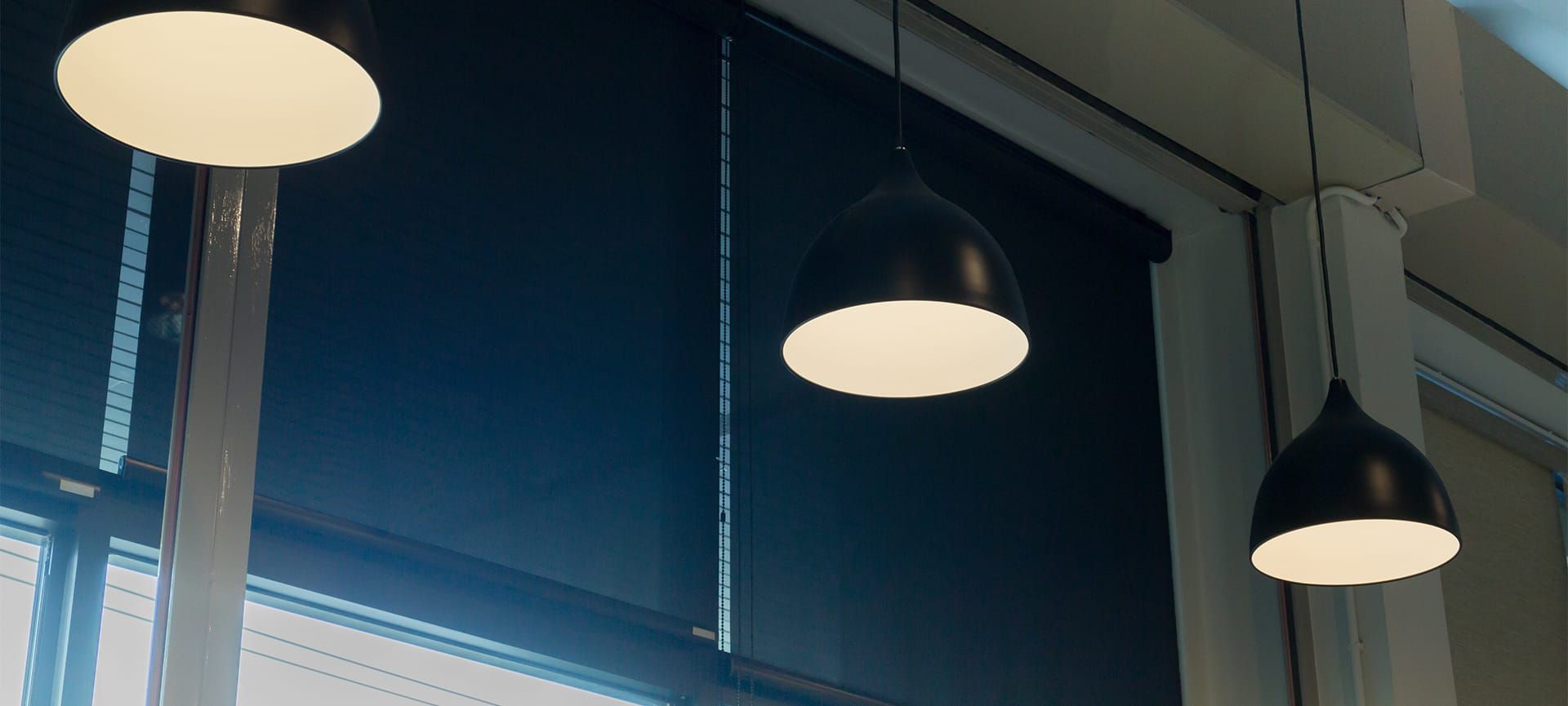 Three pendant lights hanging above a window with dark blinds