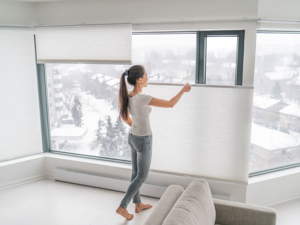 Woman opening a window blind in a bright living room with large windows