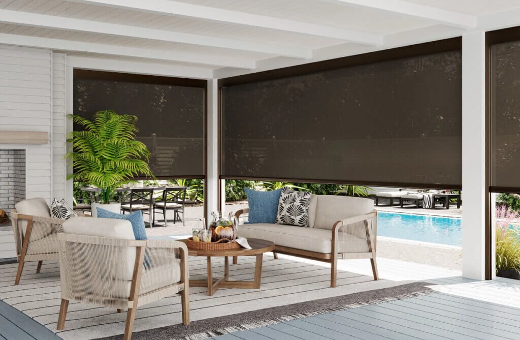 Covered patio with wicker seating, potted plant, and a pool view beyond dark roller shades.
