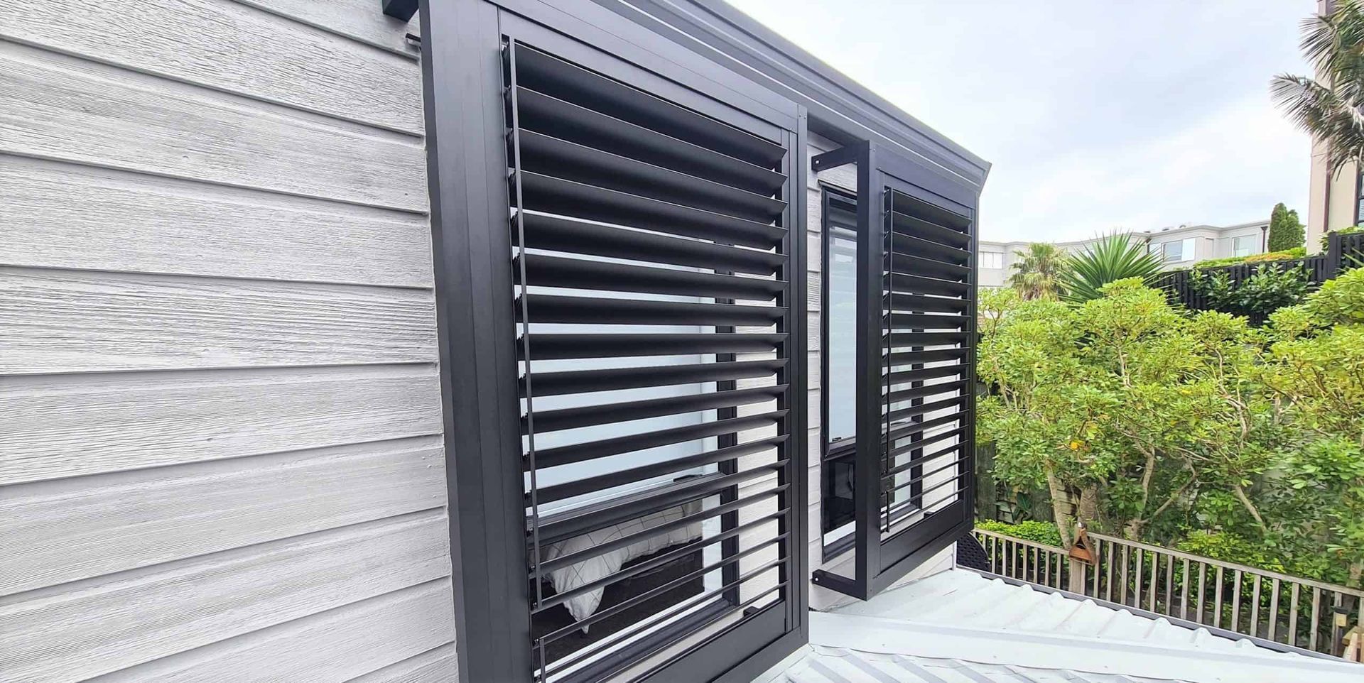 Modern house exterior with black louvered window shutters and greenery outside