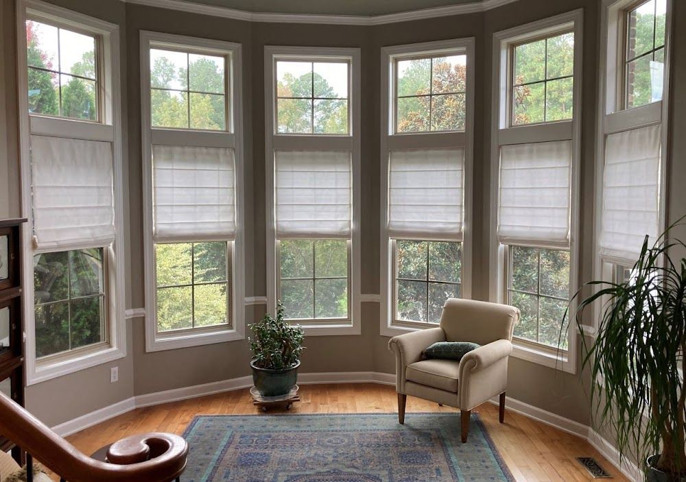 Bright bay window nook with white blinds, a beige chair, potted plant, and blue rug