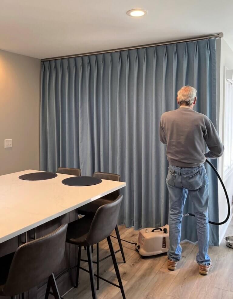 Man vacuuming floor beside a blue curtain in a modern conference room
