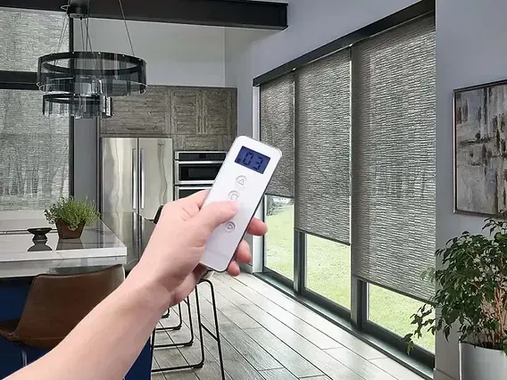 Hand holding a remote toward smart blinds in a bright modern room
