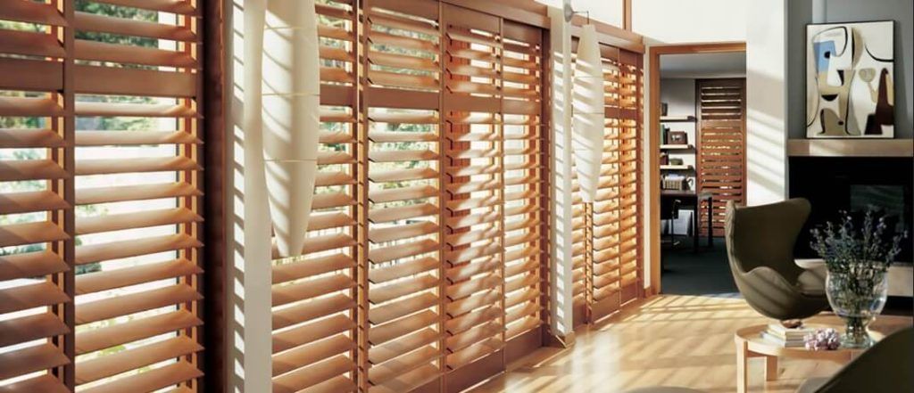Living room with large windows covered by wooden plantation shutters and warm sunlight