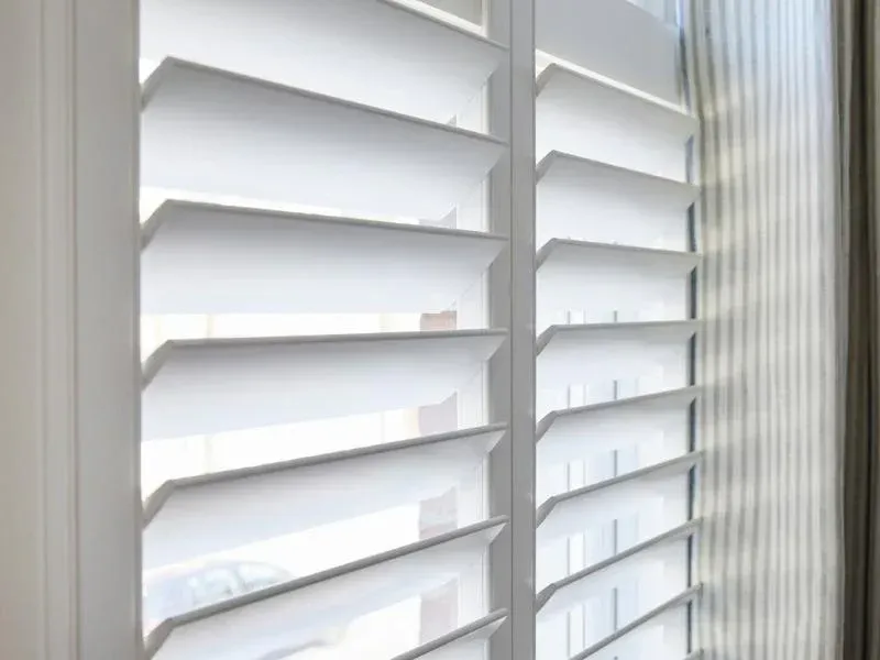 White plantation shutters filtering daylight beside a ribbed glass window panel