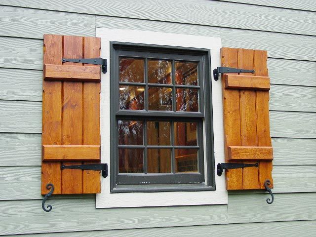 White-framed window with black muntins and orange wooden shutters on gray siding