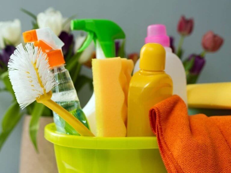 Cleaning supplies in a green bucket with sponge, spray bottles, brush, and orange cloth