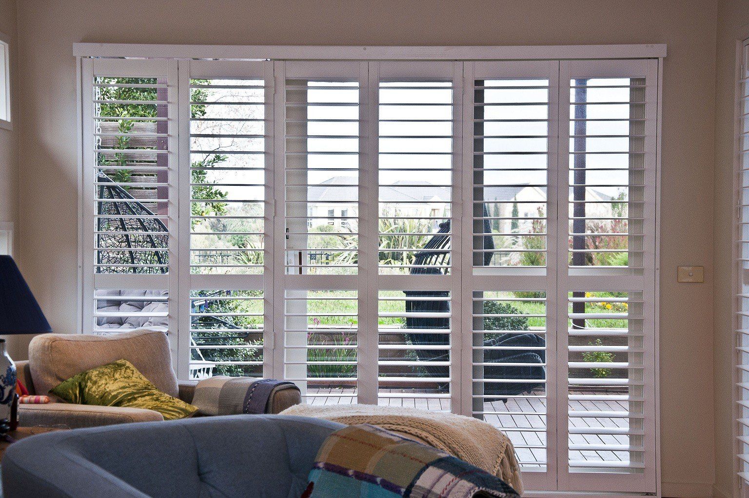 Living room with large white plantation shutters opening to a patio and greenery outside