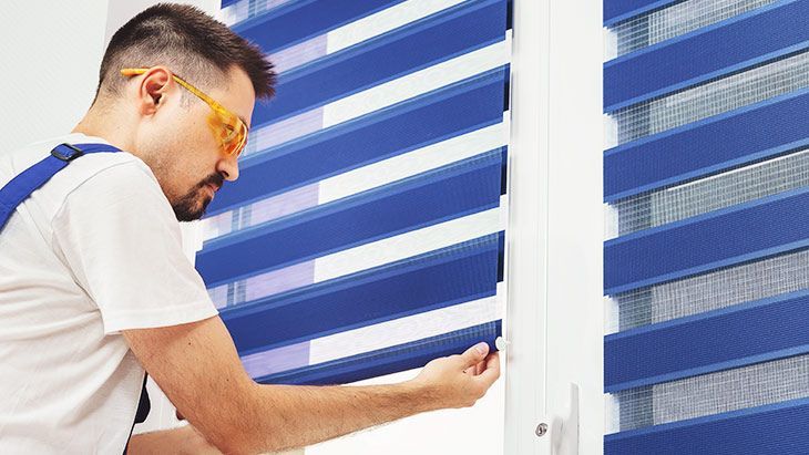 Man adjusting blue striped window blinds in a bright room