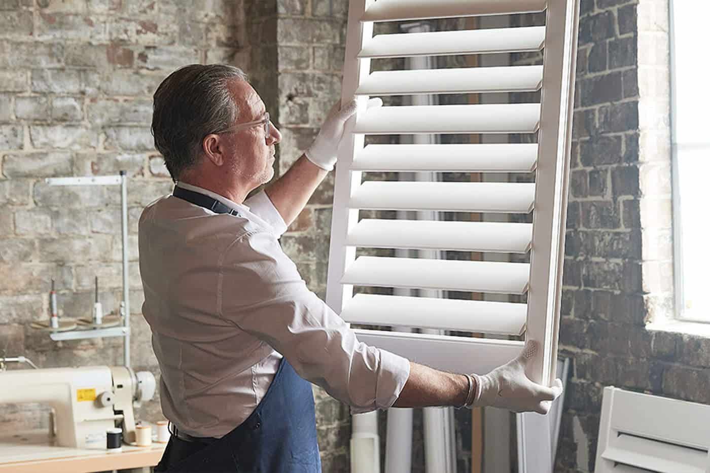 Man adjusting white window blinds in a brick-walled room near a bright window