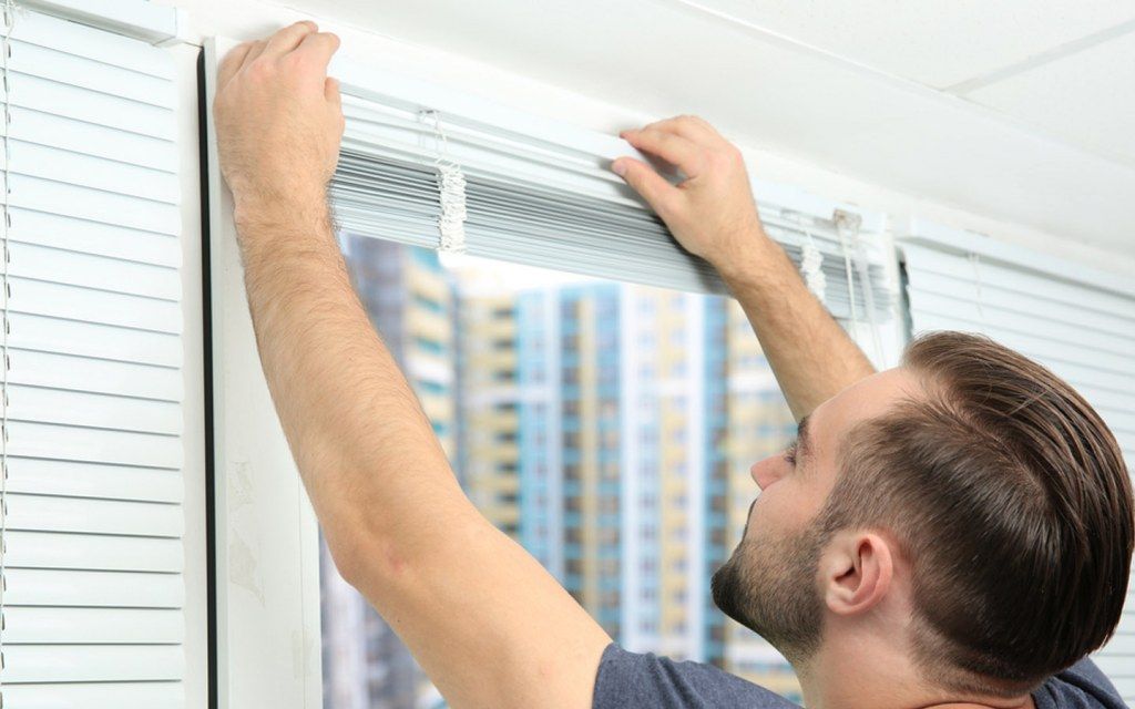 Man adjusting white window blinds by a bright window