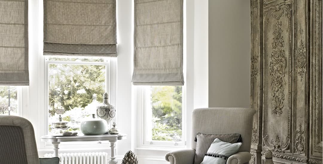 Bright living room with layered window shades, a small table, and a patterned armchair by a window.