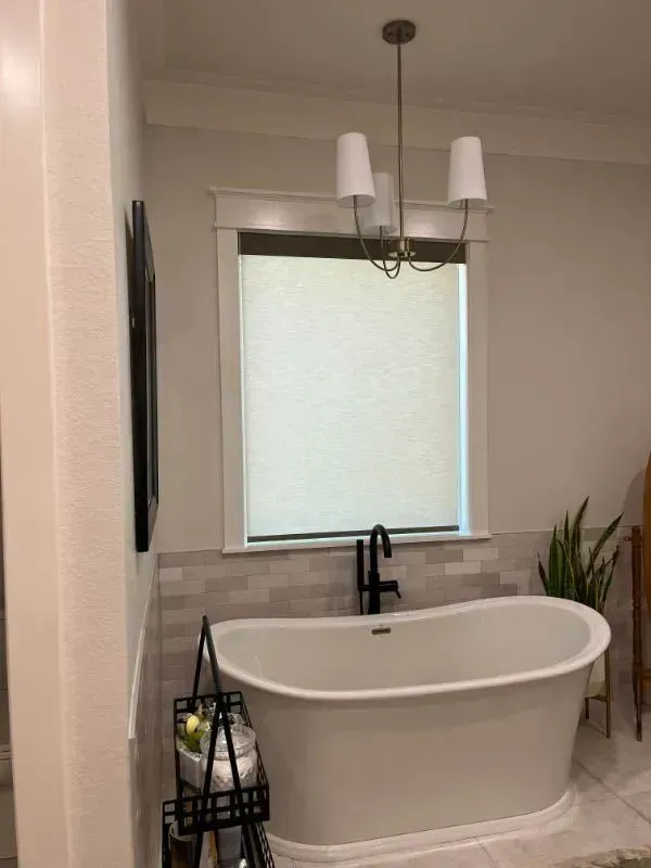 Modern bathroom with a freestanding tub, black fixtures, tiled wall, and pendant lights beneath a window.