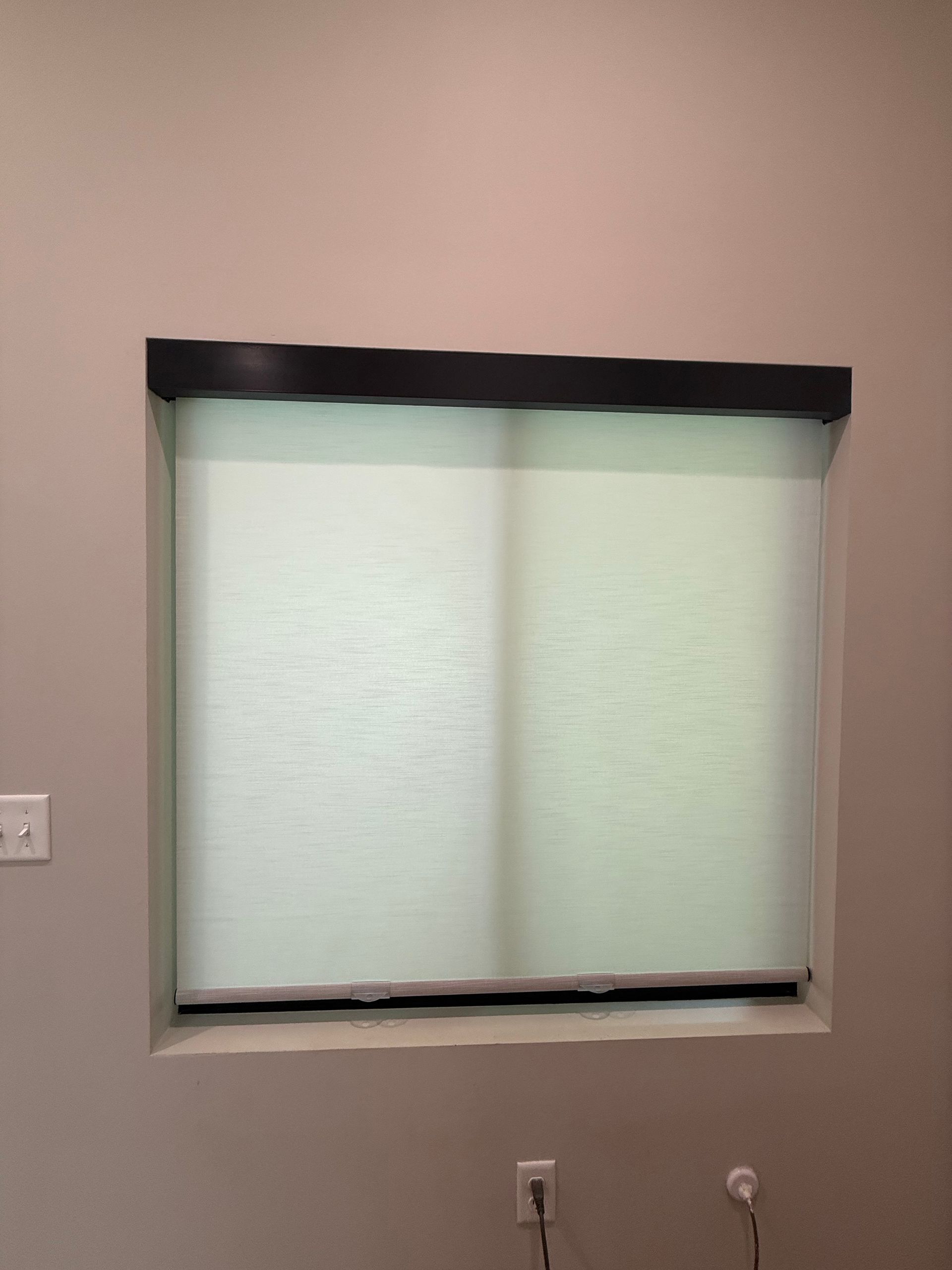 Closed window with white blinds and black valance on a beige wall