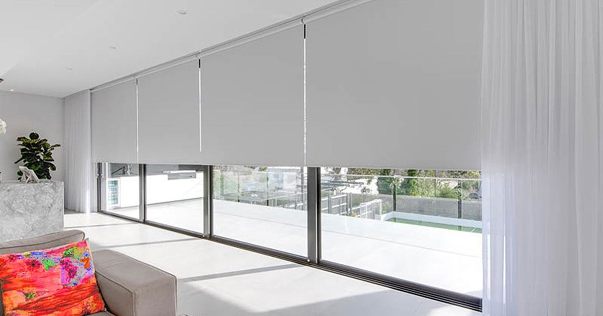 Bright living room with large windows covered by gray roller blinds and a colorful sofa cushion