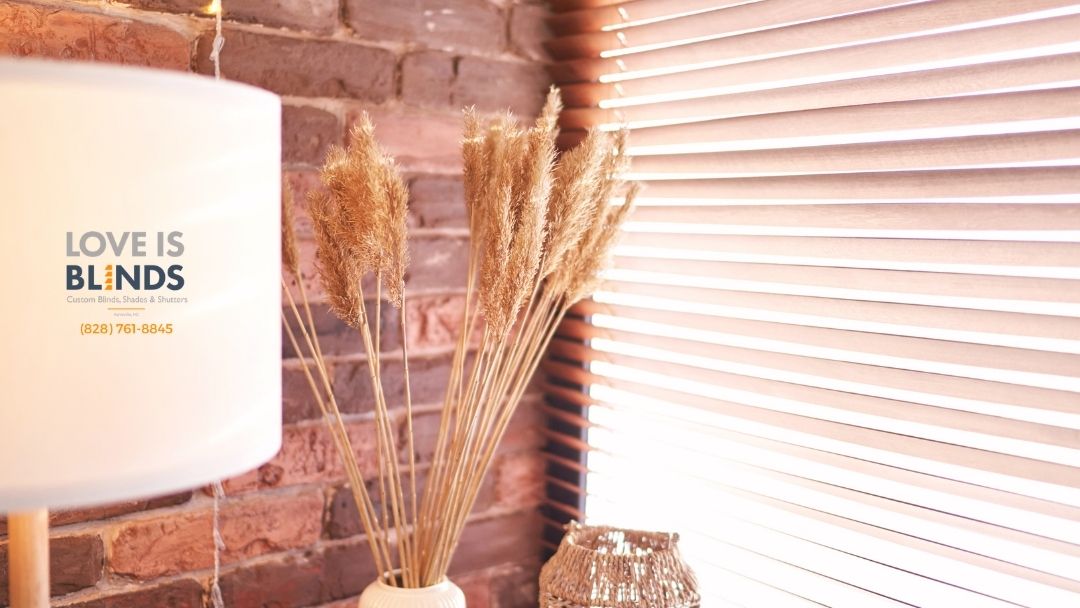 Lamp with “LOVE IS BLINDS” text beside a vase of wheat near brick wall and bright window blinds