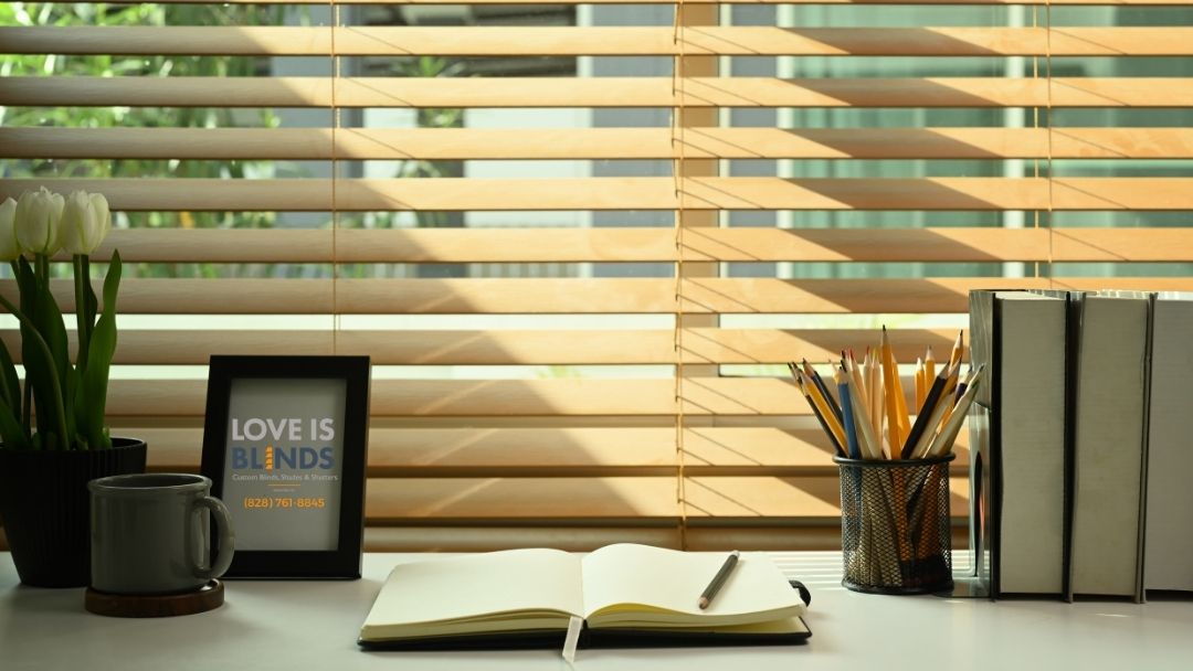 Desk by window with open notebook, mug, framed sign, pens, and books in warm sunlight.