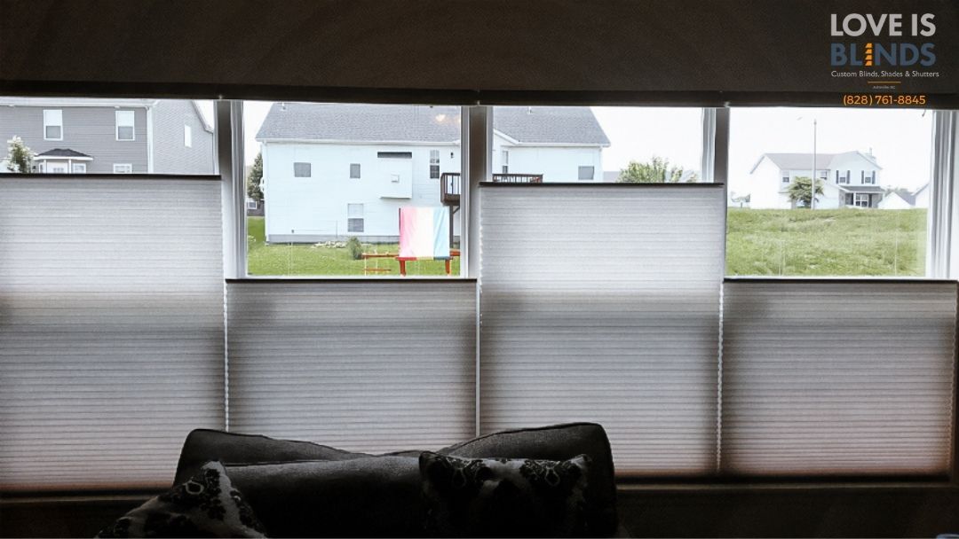 Dim living room with couch and large windows covered by blinds, showing houses outside.