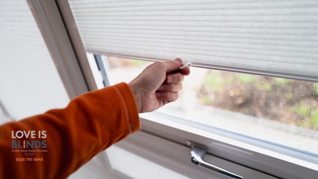 Hand pulling up a white window blind, letting light into a room