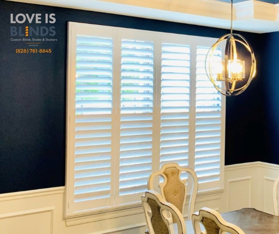 Bright dining room with white shutters, dark blue walls, and gold chandelier above ornate chairs